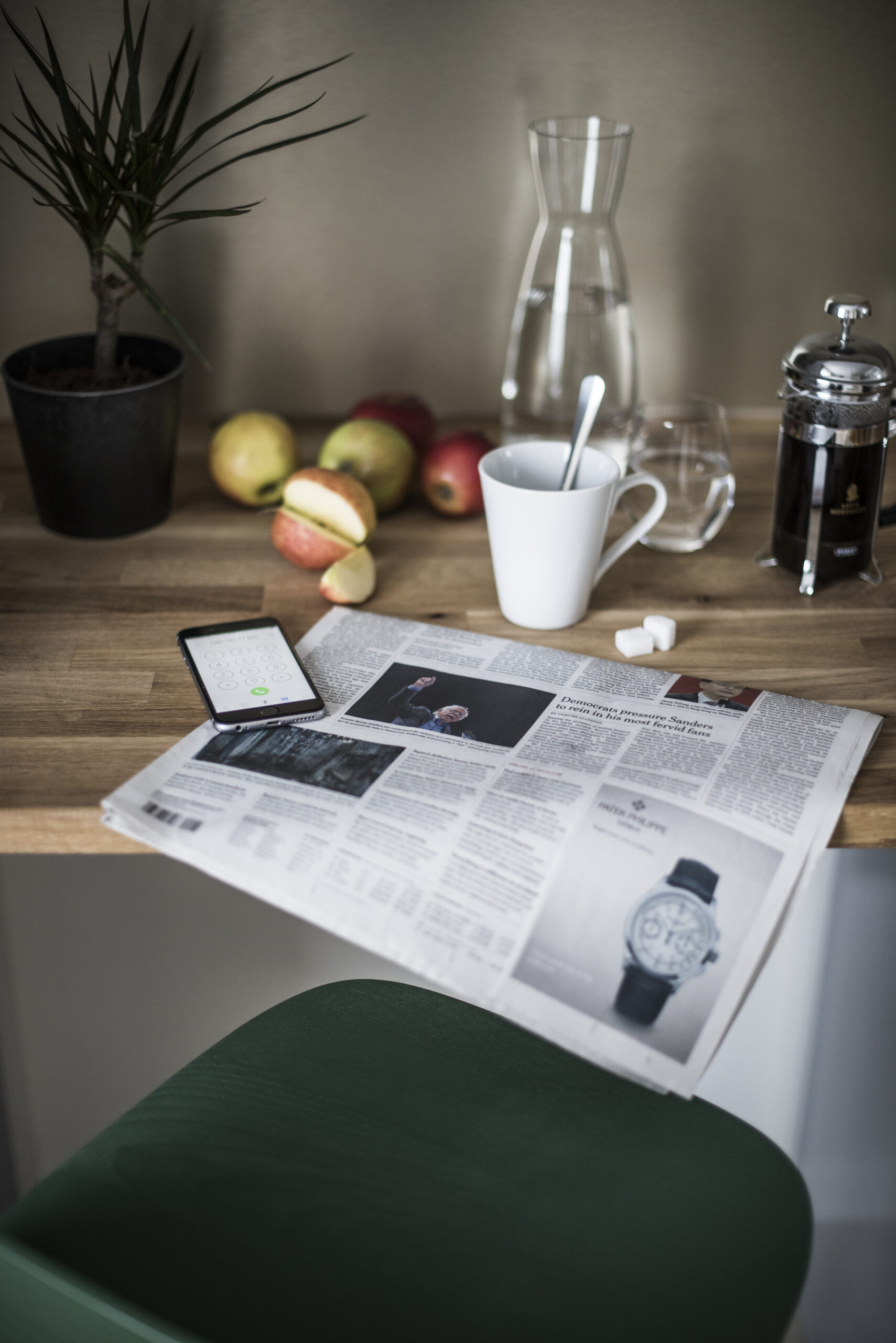 Detalj vid barbordet — French press, tidning och äpplen
