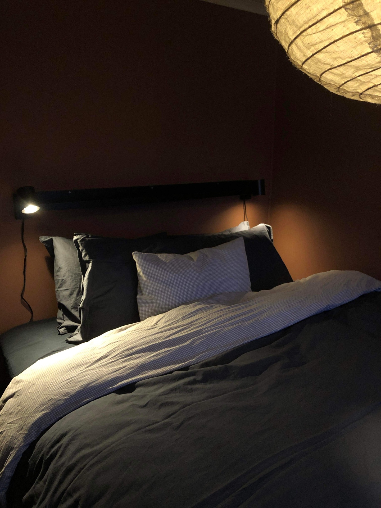 Sovrum i terrakotta med svart vägglampa och rispapperspendel