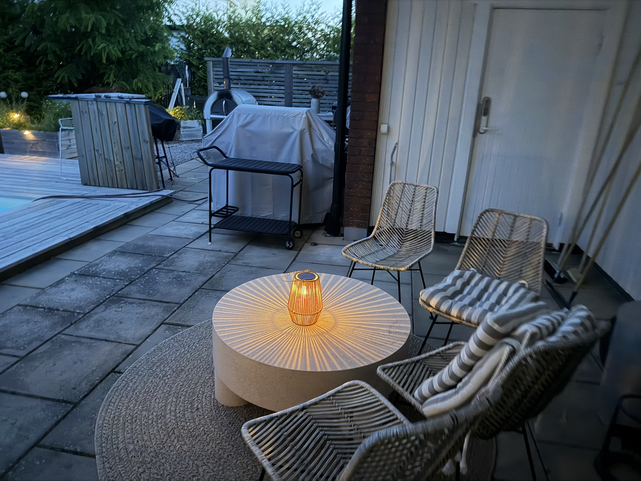Kvällslounge med lykta · grill och pizzaugn i bakgrunden